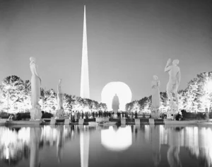 The Trylon and Perisphere lit at night behind classical statues reflected in a pool at the 1939 New York World's Fair