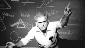 Julius Sumner Miller pointing upward with one finger raised, in front of a blackboard covered with diagrams and the names Apollonius, Newton, Galileo and Bernoulli