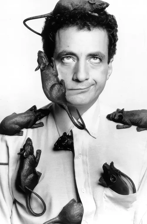 Paul Zaloom in a white shirt with eight model rats climbing over his head, shoulders and chest