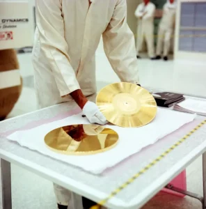 A gloved technician in a clean suit handling the Voyager Golden Record and its cover on a table in a NASA clean room
