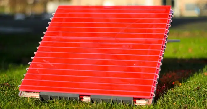 The 'artificial leaf' solar reactor, a flat red square panel, sits on a grassy lawn outdoors, propped up to face the sun.