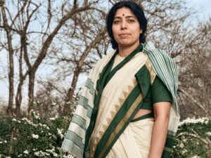 A restored and colorized historical portrait of Janaki Ammal, the first Indian woman to earn a PhD in Botany. She is standing outdoors, wearing a traditional sari, representing her pioneering work in plant genetics.