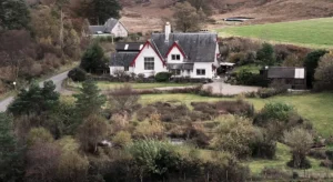 A white cottage in a sheltered Highland glen surrounded by planted trees and rough hillside
