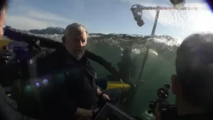 Dr Bruce Robison sitting inside a submersible as it lowers into the ocean with the water line visible across the glass.