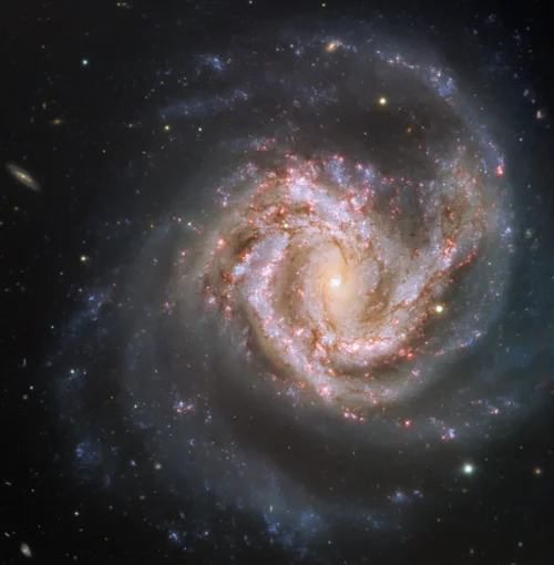 A spiral galaxy seen face on against a black sky, its bright core surrounded by blue arms streaked with pink star-forming regions, with a few foreground stars scattered around it.